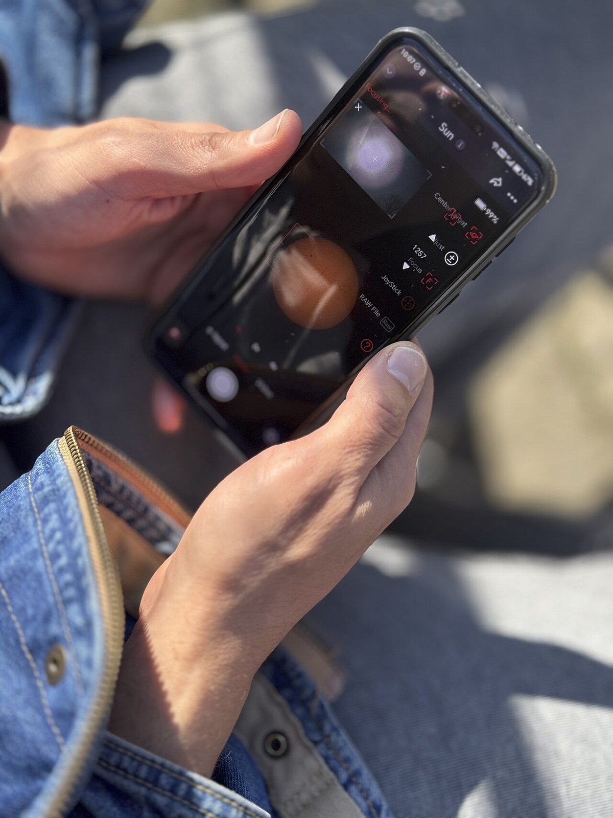 A person holding a smartphone with an app open, outdoors on a sunny day
