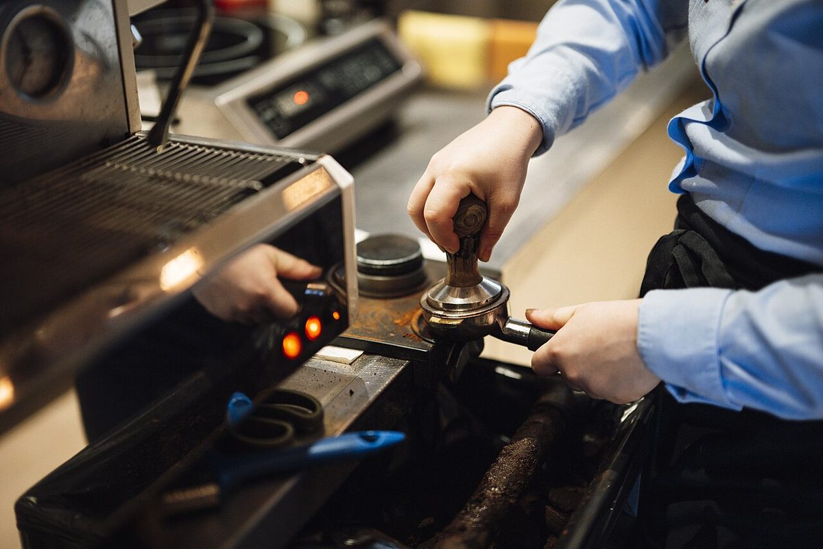 A barista tamping espresso at a coffee-shop counter in the morning