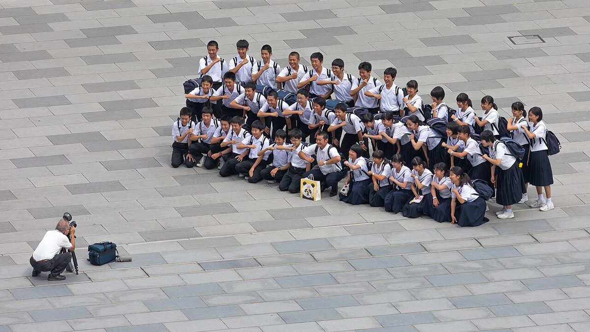 A photographer taking a group photograph of smiling students outdoors